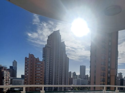 City skyline with tall buildings under a bright sun and blue sky.
