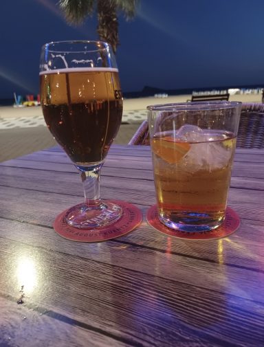 Two drinks on a wooden table; a beer in a glass and a cocktail with ice.