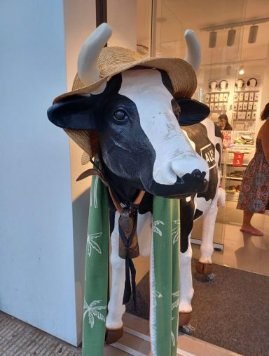 A decorative cow statue wearing a straw hat and standing on a green patterned base.