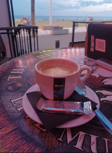 A cup of coffee on a table with a seaside view in the background.